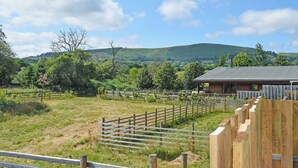 A rural landscape with a wooden fence, a small building with a metal roof, and a hill in the background. - 3 bedroom accommodation in Llandrindod Wells (Llandrindod Wells)