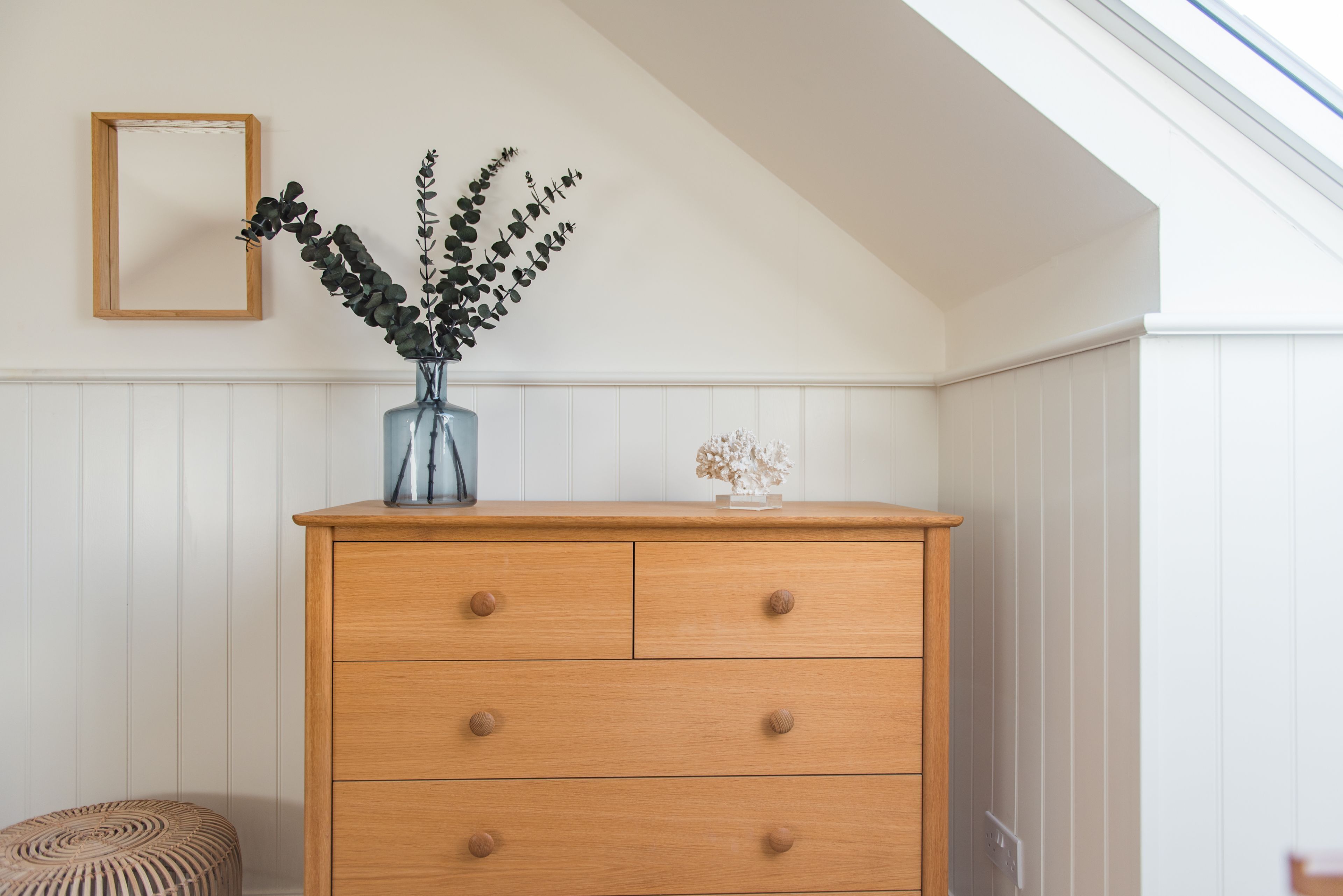 A wooden dresser with drawers, a vase with a plant, and a small decorative item on top.