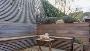 A wooden deck with a small table and benches, surrounded by a wooden wall and greenery. - Liberty Cottage, Broadstairs (Broadstairs)
