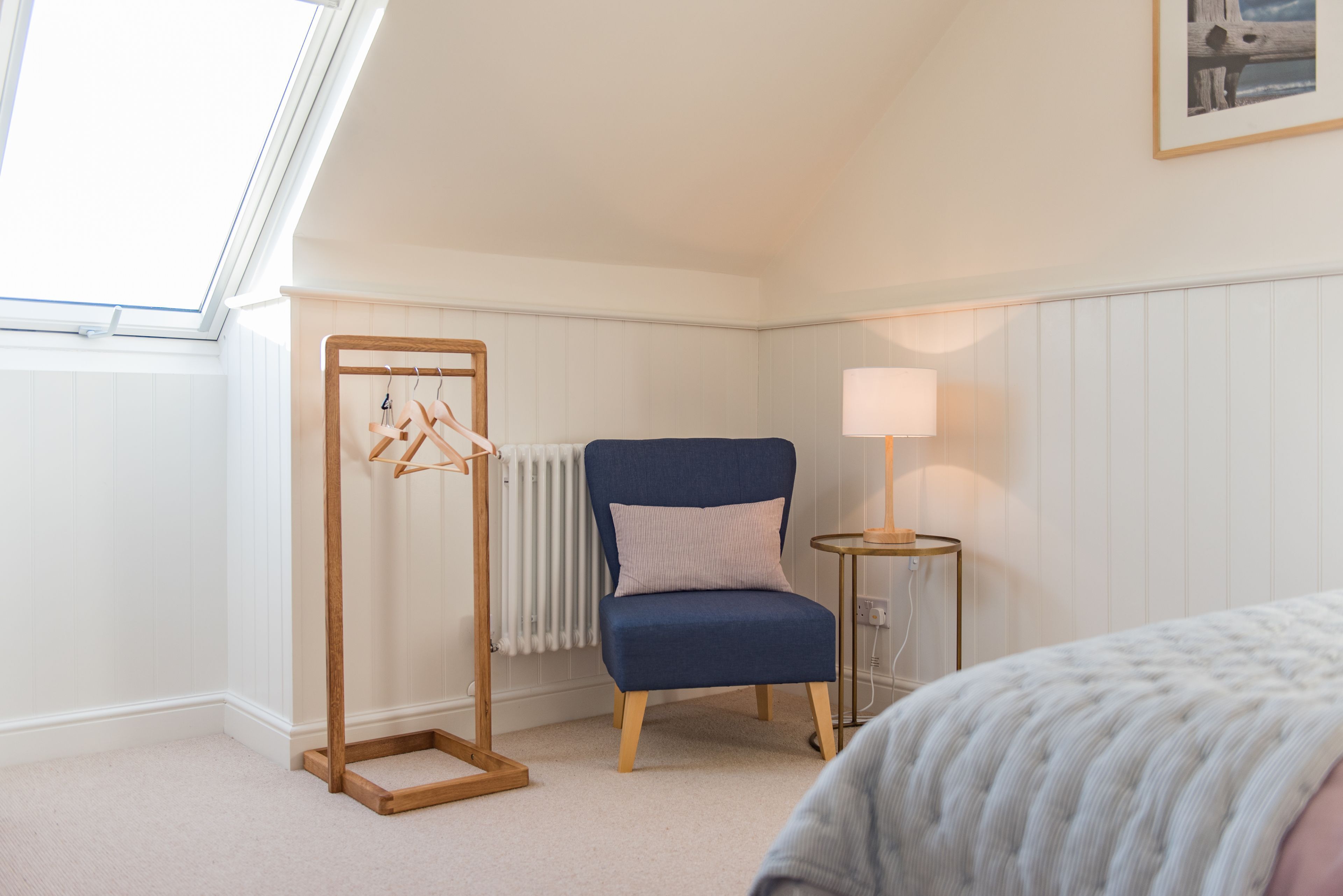 Une chambre avec un puits de lumière, une chaise bleue, une table de chevet avec une lampe et un radiateur.
