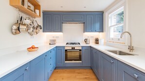 A kitchen with blue cabinets, white countertops, a built-in oven, and a stainless steel sink. - Liberty Cottage, Broadstairs (Broadstairs)