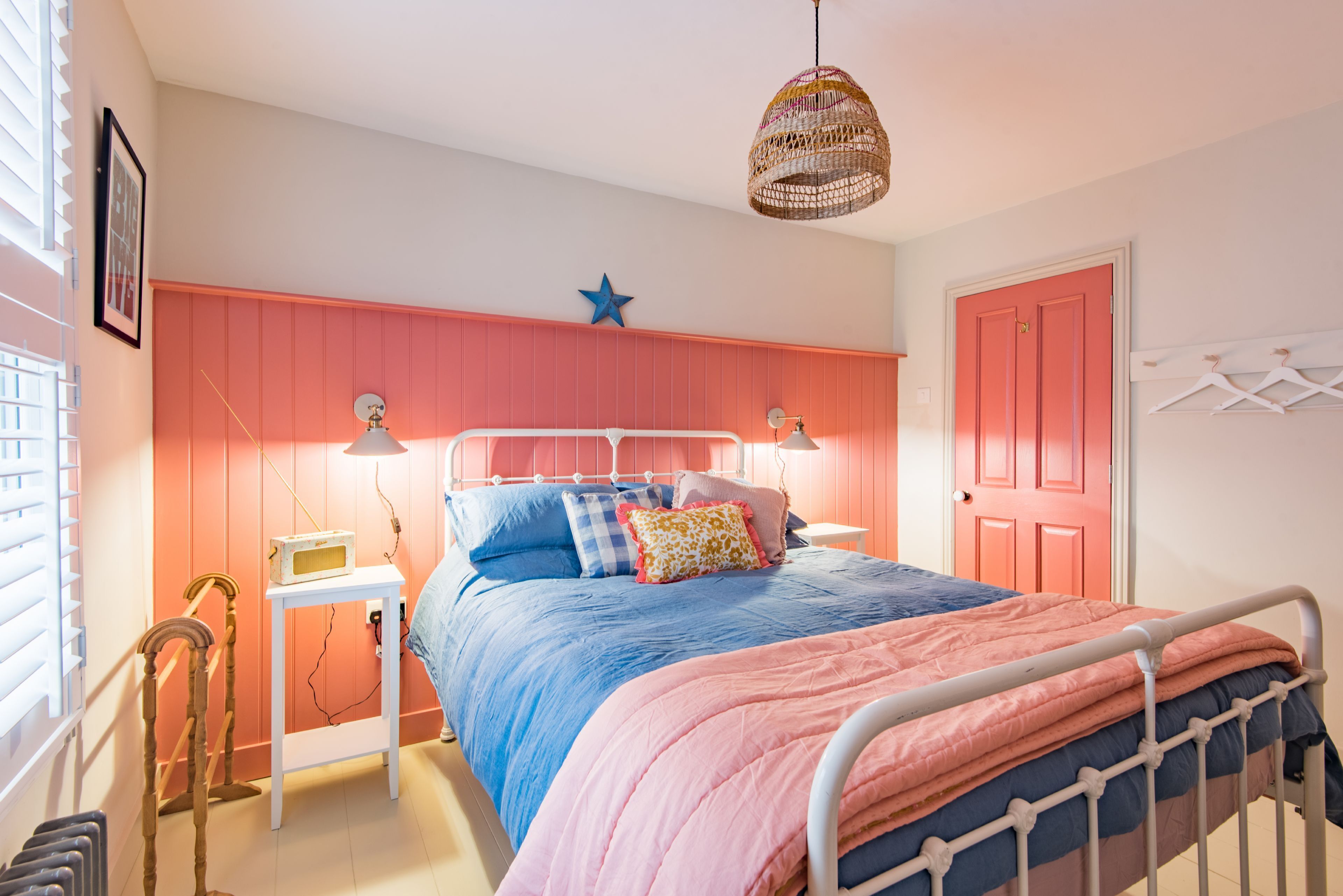 Een slaapkamer met een bed, nachtlampjes, een hanglamp, een ster decoratie, een deur en een radiator.