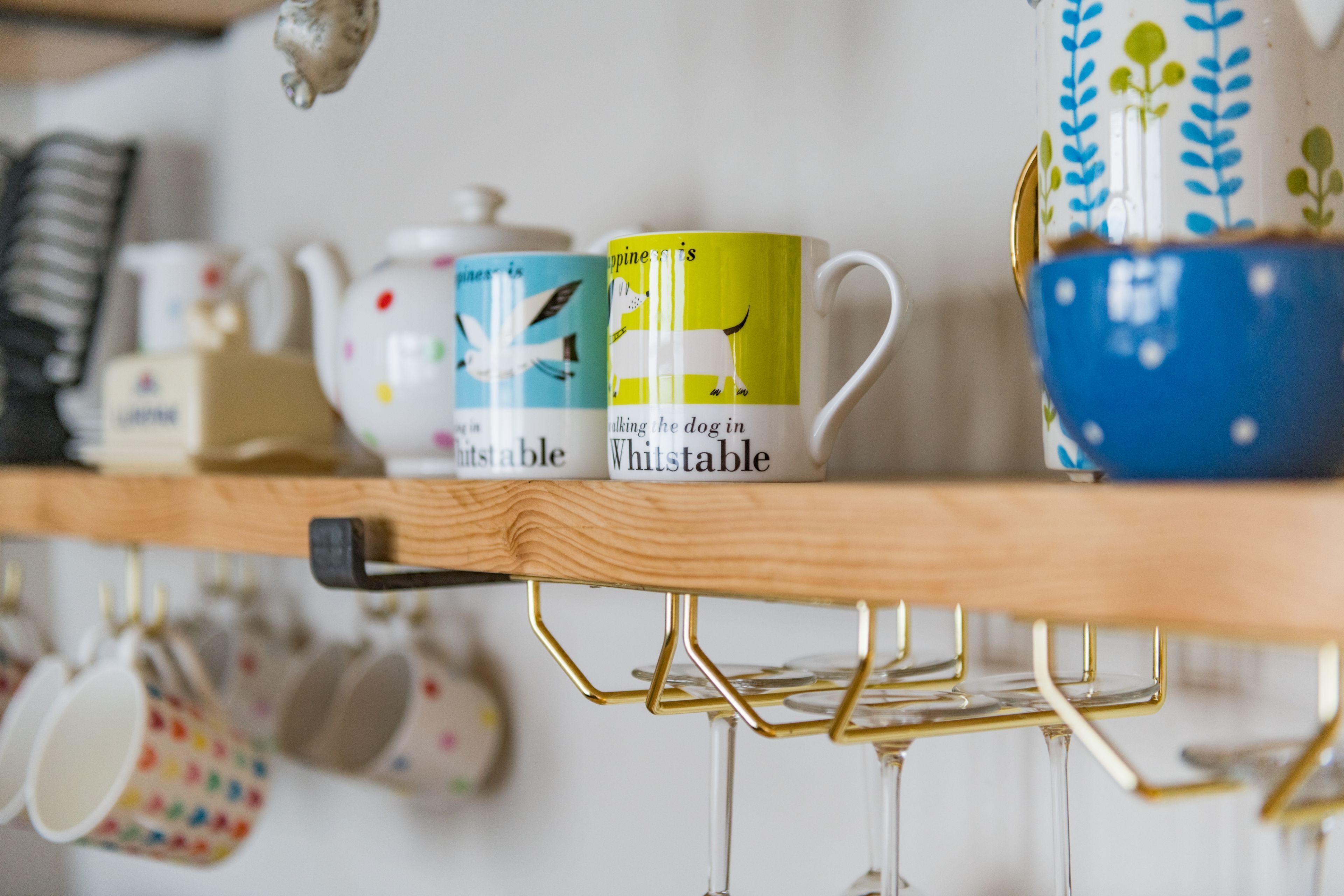 A shelf with various kitchenware items including mugs, a teapot, and a bowl.