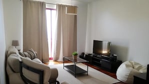 Un soggiorno moderno con un divano, un tavolino, una televisione e un pouf.