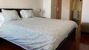Un letto rifatto con una coperta a motivi, una lampada da comodino e una porta in legno che dà su un bagno.