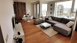 A modern living room with a sofa, coffee table, and a dining area with a table and chairs. - City view from 27th floor, free parking, keyless (Bratislavský kraj)