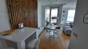 A modern living space with a dining area, a white sofa, and a view of the city through large windows. - City view from 27th floor, free parking, keyless (Bratislavský kraj)