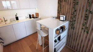 A compact kitchen with white cabinetry, a small island with a white countertop, and a chair. There is a sink, a stove, and a refrigerator. - City view from 27th floor, free parking, keyless (Bratislavský kraj)