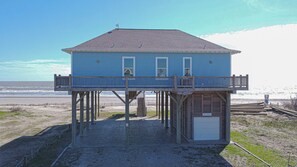 A blue house with a balcony on stilts, located near a beach.
