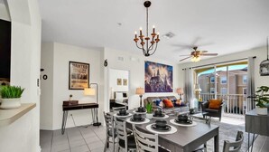 A modern dining area with a chandelier, ceiling fan, and a large window with a view of buildings. - Wizarding Retreat: Enchanted Harry Potter Condo (Kissimmee)