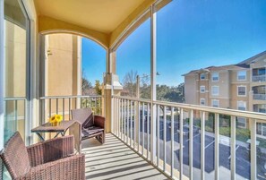 Enjoy the view from this balcony with a glass door, two wicker chairs, and a small table.