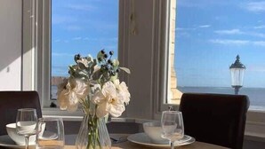 A dining table with a vase of flowers and wine glasses, set against a view of the sea. - Apartment 14, The Moorings  Beachfront & panoramic sea views (Filey)