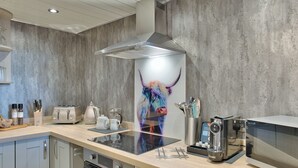 Une cuisine moderne dotée d’une hotte en acier inoxydable, d’un four encastré, d’un four à micro-ondes et d’une machine à café. On y trouve un plan de travail en bois, un porte-couteaux et une bouilloire.