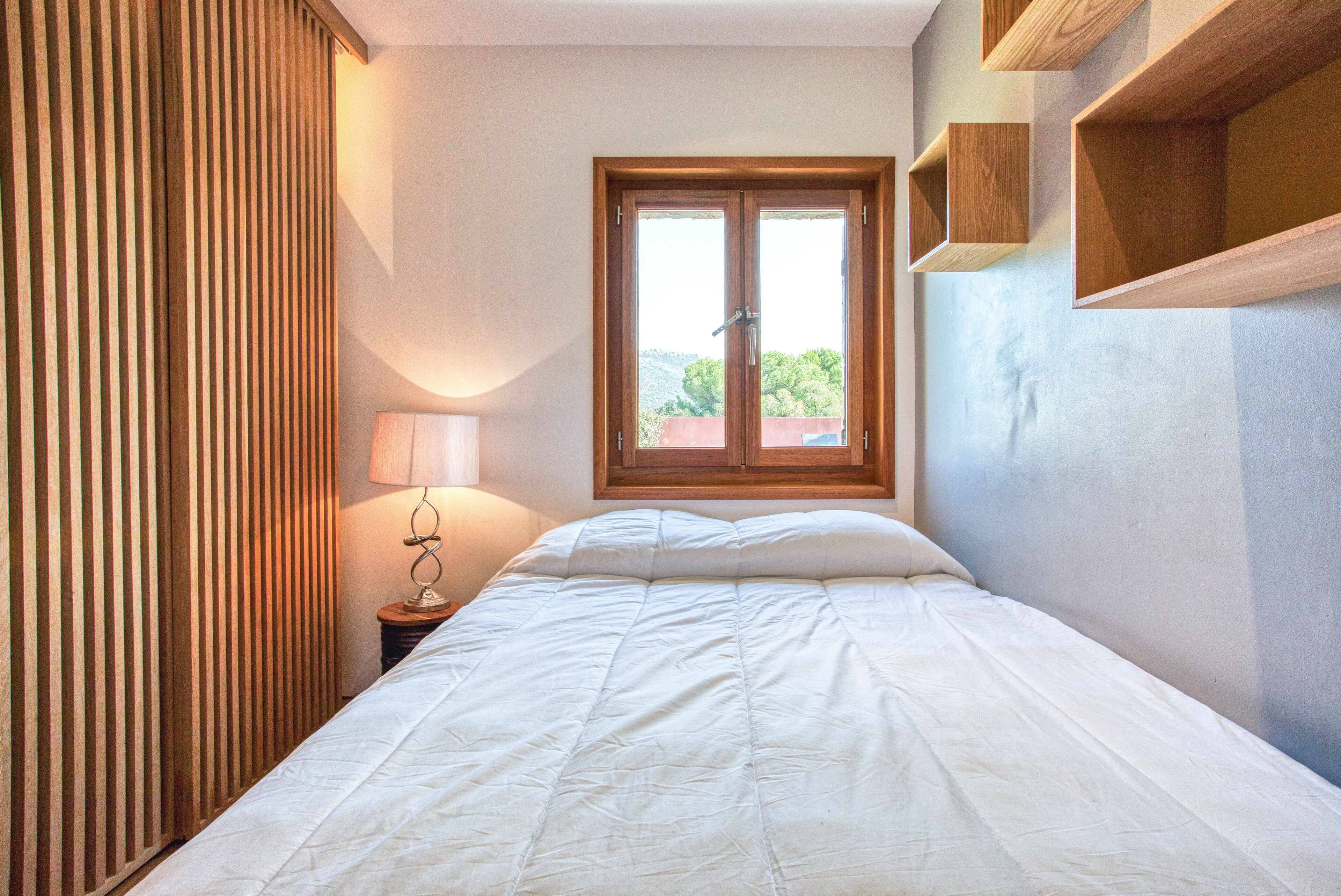 Une chambre à coucher avec un lit, une fenêtre, une lampe et des étagères en bois.