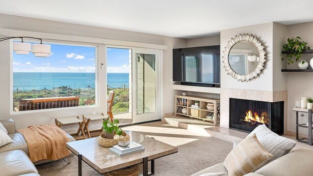 A spacious living room with a large TV, a fireplace, and a view of the ocean through large windows. - Oceanfront - Ocean Views - Pool  Spa - Pickleball - Walk To All - Renovated (Solana Beach)