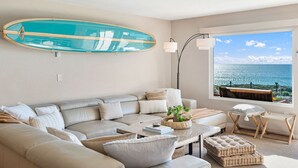 A modern living room with a large window offering a view of the sea. - Oceanfront - Ocean Views - Pool  Spa - Pickleball - Walk To All - Renovated (Solana Beach)