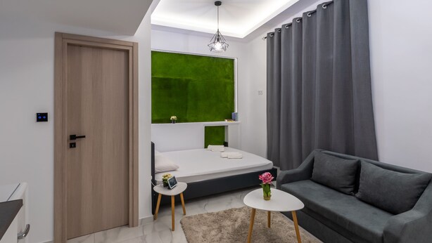 A modern bedroom with a bed, a grey sofa, a small white table, and a green accent wall.