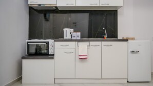 A modern kitchen with white cabinets, a built-in microwave, a coffee maker, and a mini fridge.