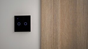 A black switch with two illuminated blue circles on a white wall next to a wooden surface.