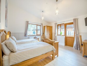 A bedroom with two beds, wooden furniture, a window with curtains, and a view of the outside.