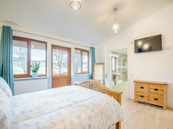 Un dormitorio con una cama, un aparador de madera, un televisor y un baño visible a través de una puerta abierta.