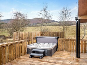 A hot tub on a wooden deck with a view of hills.