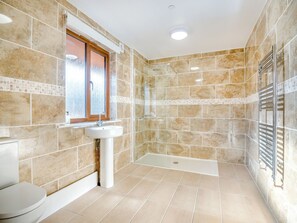 A bathroom with a shower, sink, and toilet, featuring beige tiles and a window.