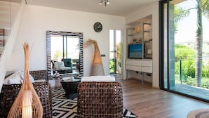 Ein modernes Wohnzimmer mit Rattanmöbeln, einem großen Spiegel und Blick auf Grünflächen.