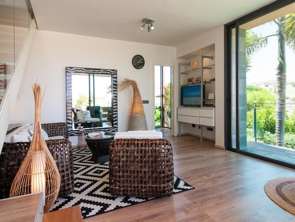 A modern living room with wicker furniture, a large mirror, and a view of greenery outside. - Lagos 20 by VillaGranCanaria (San Bartolomé de Tirajana)