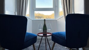 A room with two blue chairs facing a window with a view of trees. A small table with a bottle and a glass is in front of the window. - 3 bedroom accommodation in Larkhall (Larkhall)
