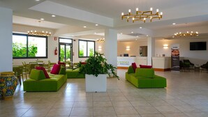 Un hall de hotel con sofás verdes, una recepción y un ventanal con vistas a la vegetación.