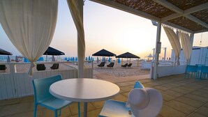 Un patio frente a la playa con una mesa, sillas, sombrillas y vista al mar.