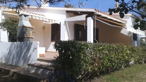 A house with a tiled roof, a covered porch, and a small garden area with steps leading to the entrance. - Menorcan house 20 m from the sea (Binisafua)