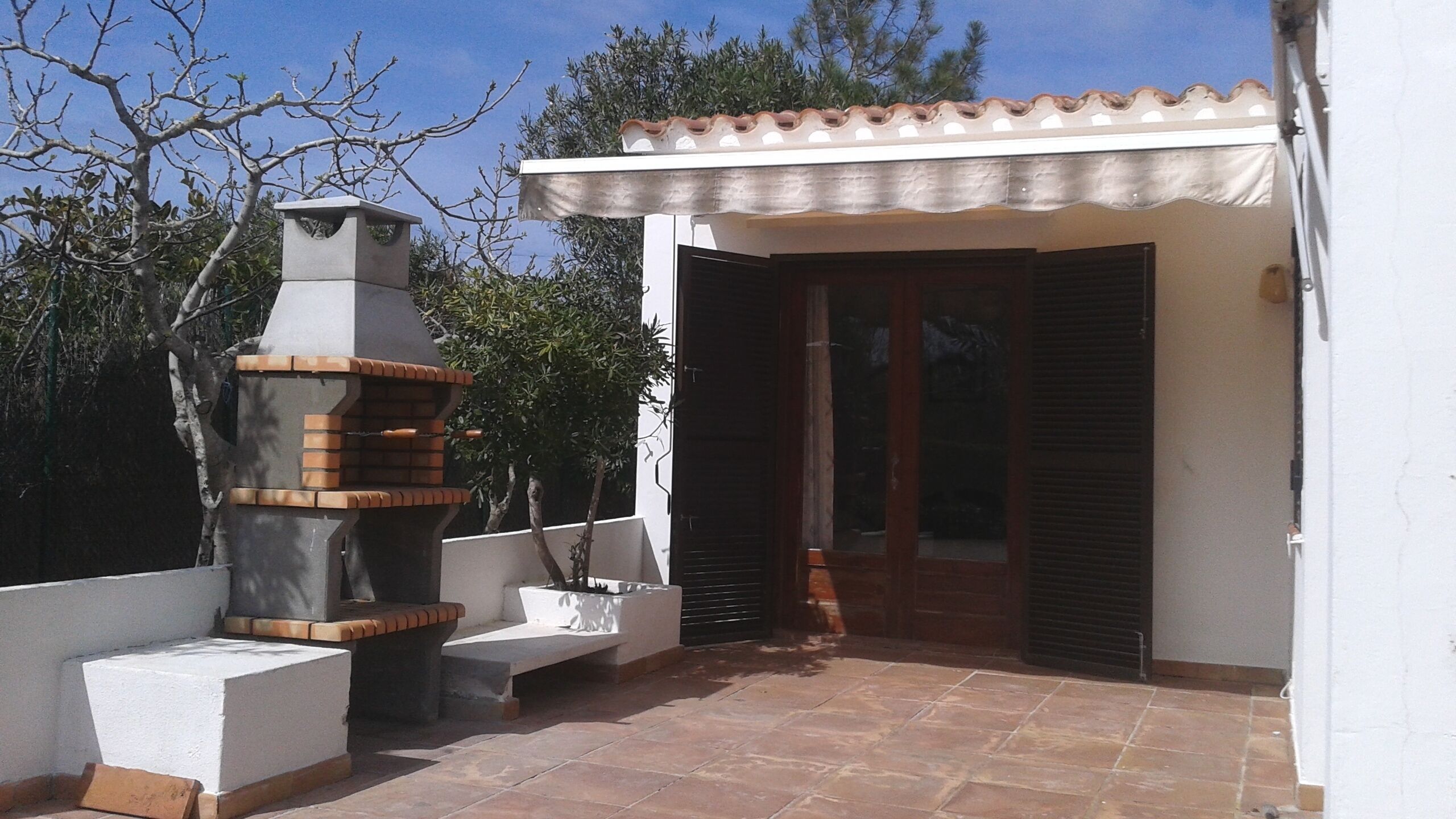 A patio with a brick oven, a white wall, and a door with shutters.