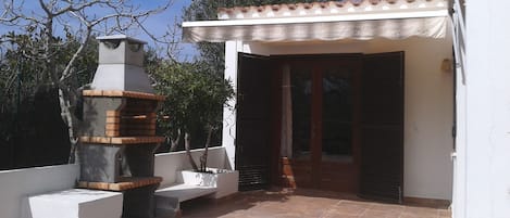 A patio with a brick oven, a white wall, and a door with shutters.