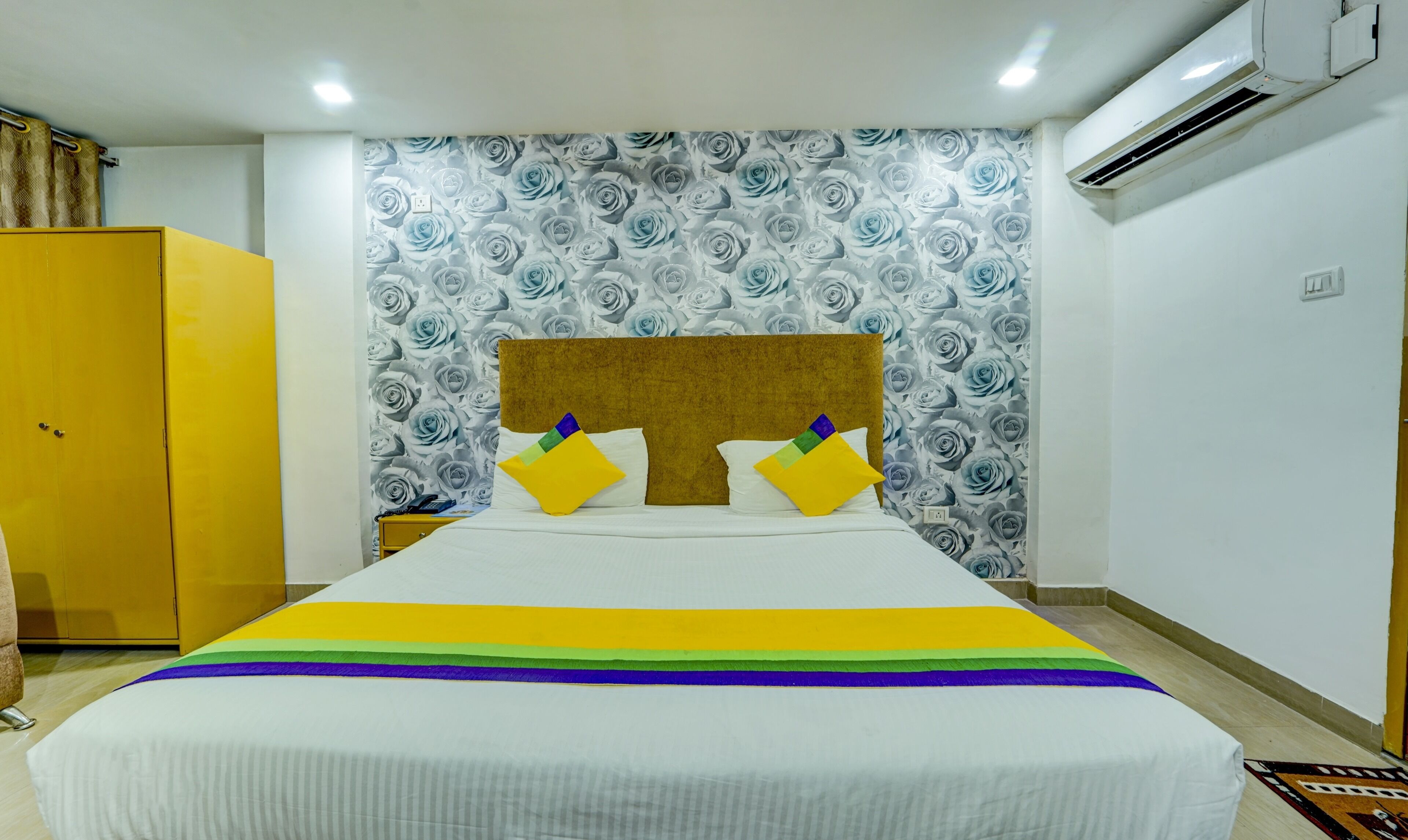 A hotel room with a bed, a wardrobe, and a wall with a floral pattern.