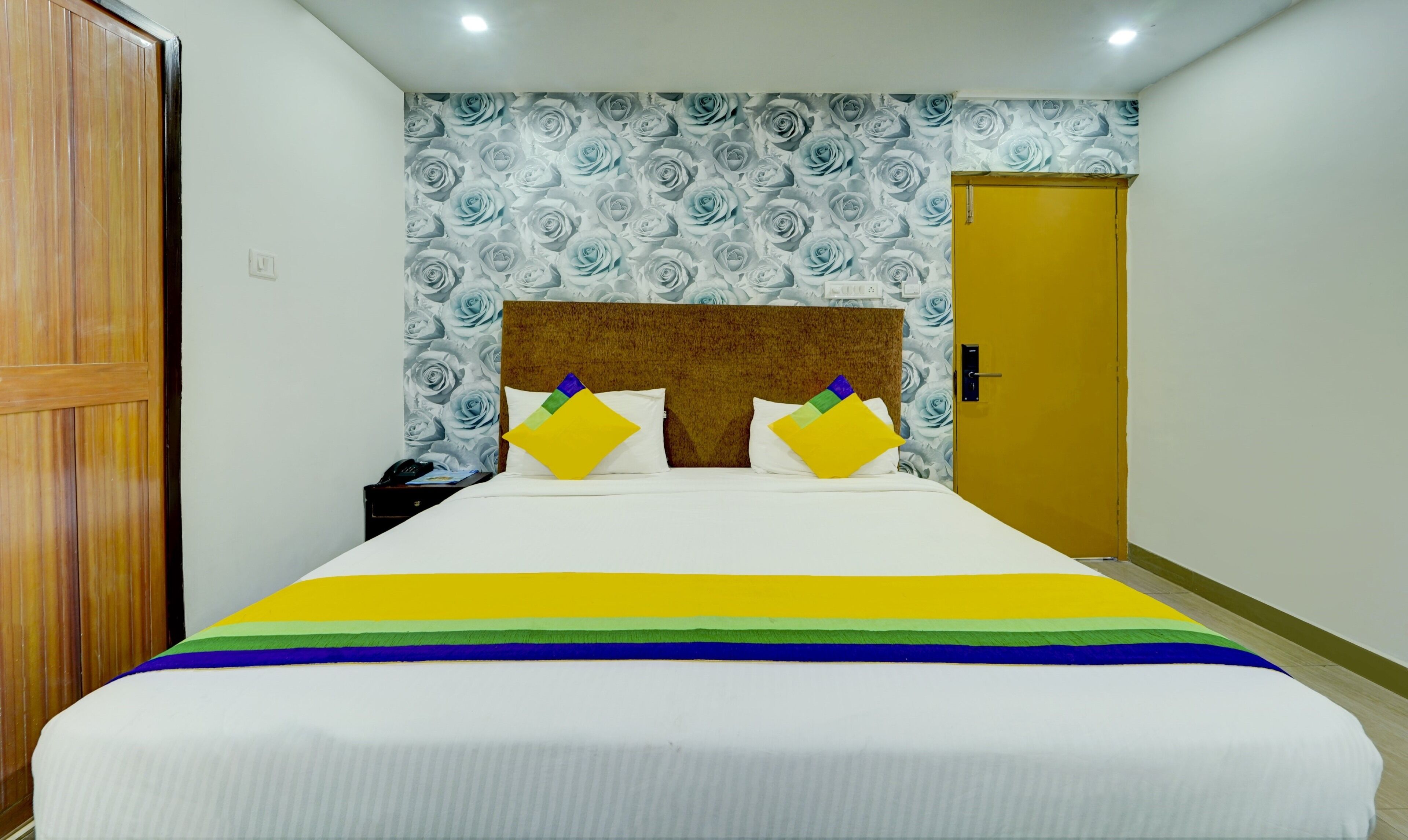 Una habitación de hotel con una cama grande, un armario de madera, un papel tapiz estampado y una puerta amarilla.