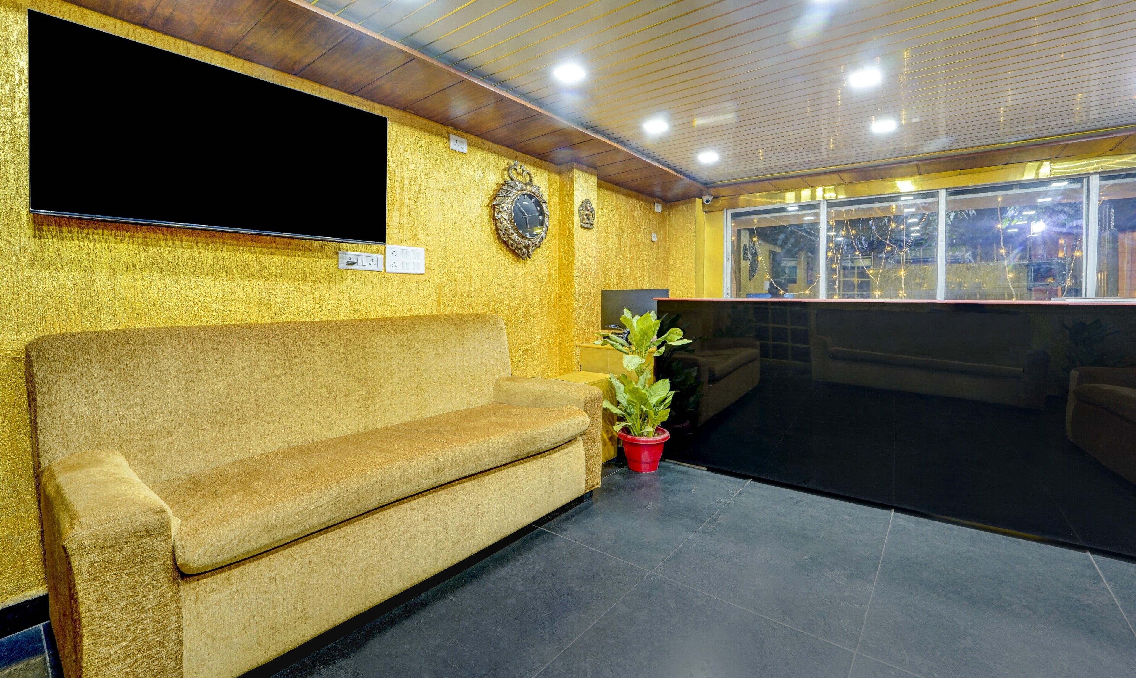 Un área de recepción con un sofá, un televisor, adornos en la pared y una ventana con luces.
