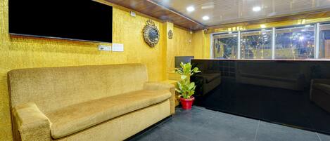 A reception area with a sofa, a TV, decorative wall pieces, and a window with lights.