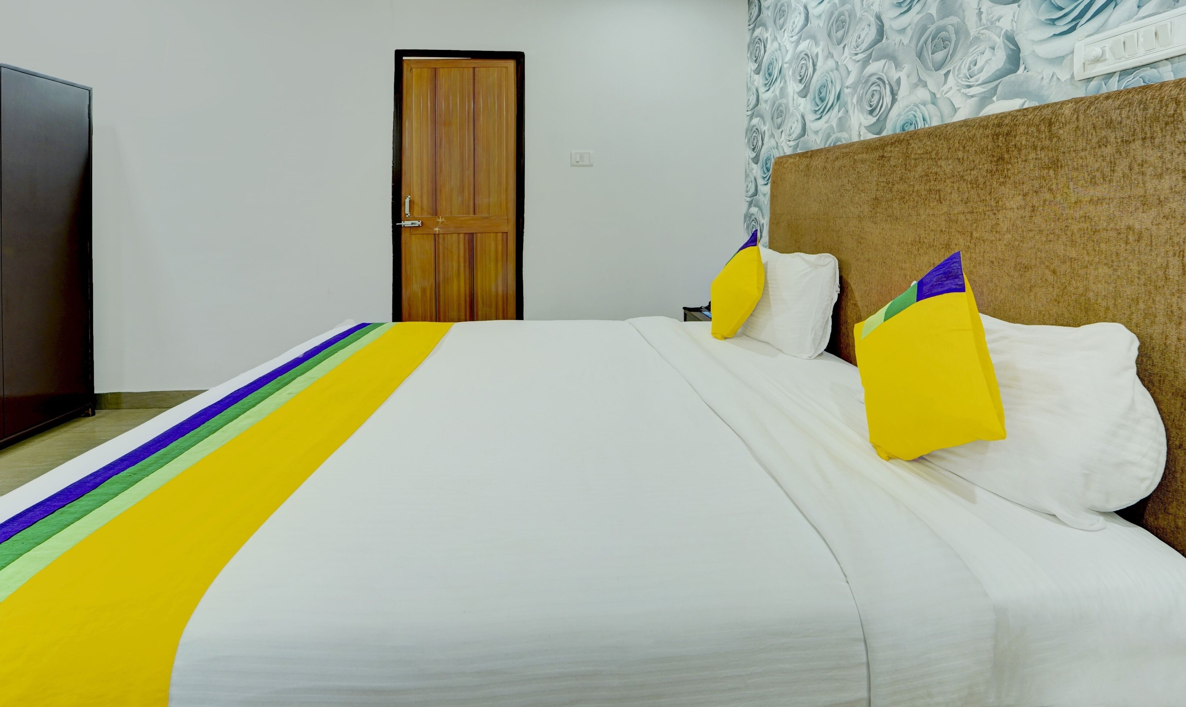 Una habitación de hotel con una cama, una puerta de madera y una pared con estampado floral.