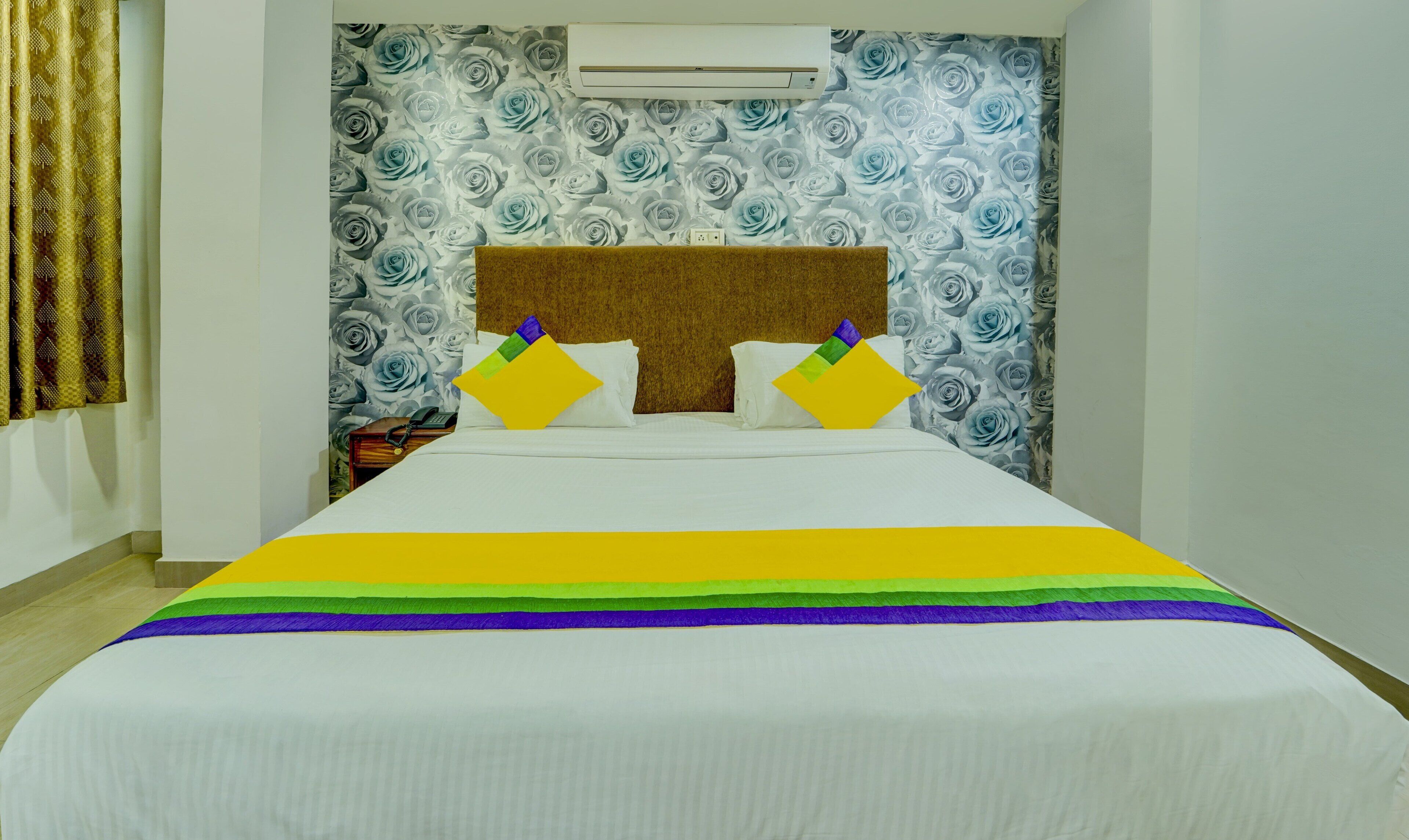 Habitación de hotel con cama, cabecera, aire acondicionado de pared y papel tapiz estampado.