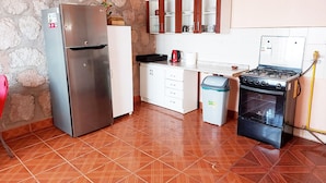 Una cocina compacta con un refrigerador de acero inoxidable, estufa a gas, gabinetes blancos y piso de baldosas.