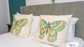A bed with two pillows featuring a butterfly design, a grey upholstered headboard, and a small plant in the background. - Luke Stays -Good StationCottages (Durham)