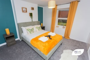 Ein Schlafzimmer mit einem Bett, Nachttischen, einem Fenster mit Vorhängen und einer Wandlampe.