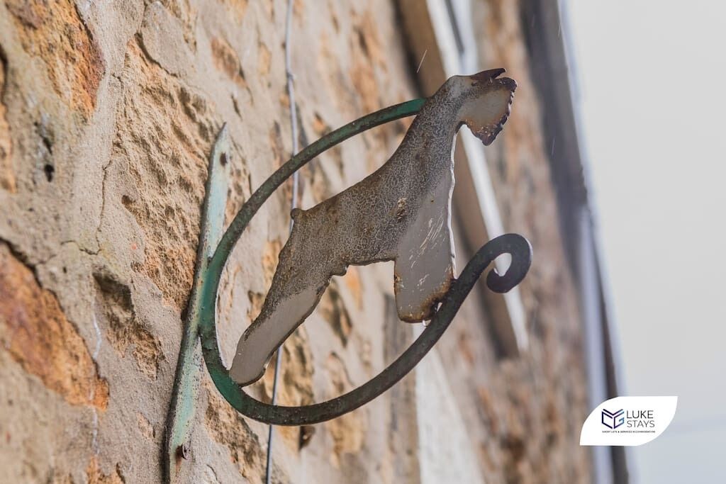 A rustic metal sculpture of a bird, possibly a rooster, attached to a weathered stone wall.