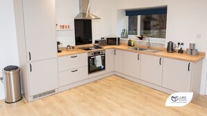 A modern kitchen with white cabinets, a stainless steel range hood, a double oven, a microwave, and a window with a view of the city. - Luke Stays -Good StationCottages (Durham)