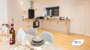 A modern kitchen with a central island, built-in oven, and a window with a view. - Luke Stays -Good StationCottages (Durham)