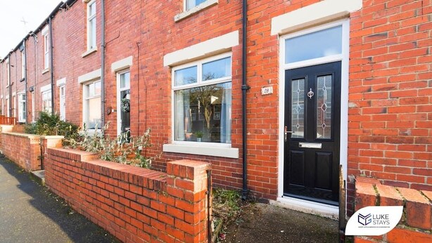 A red brick terraced house with a black front door, white-framed windows, and a small garden area. - Luke Stays - Rokeby Street (Newcastle Upon Tyne)
