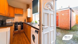A compact kitchen with wooden cabinets, a microwave, a washing machine, and a sink. - Luke Stays - Rokeby Street (Newcastle Upon Tyne)