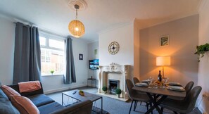 Een moderne woonkamer met een bank, een eettafel gedekt voor vier personen, een open haard en een televisie.